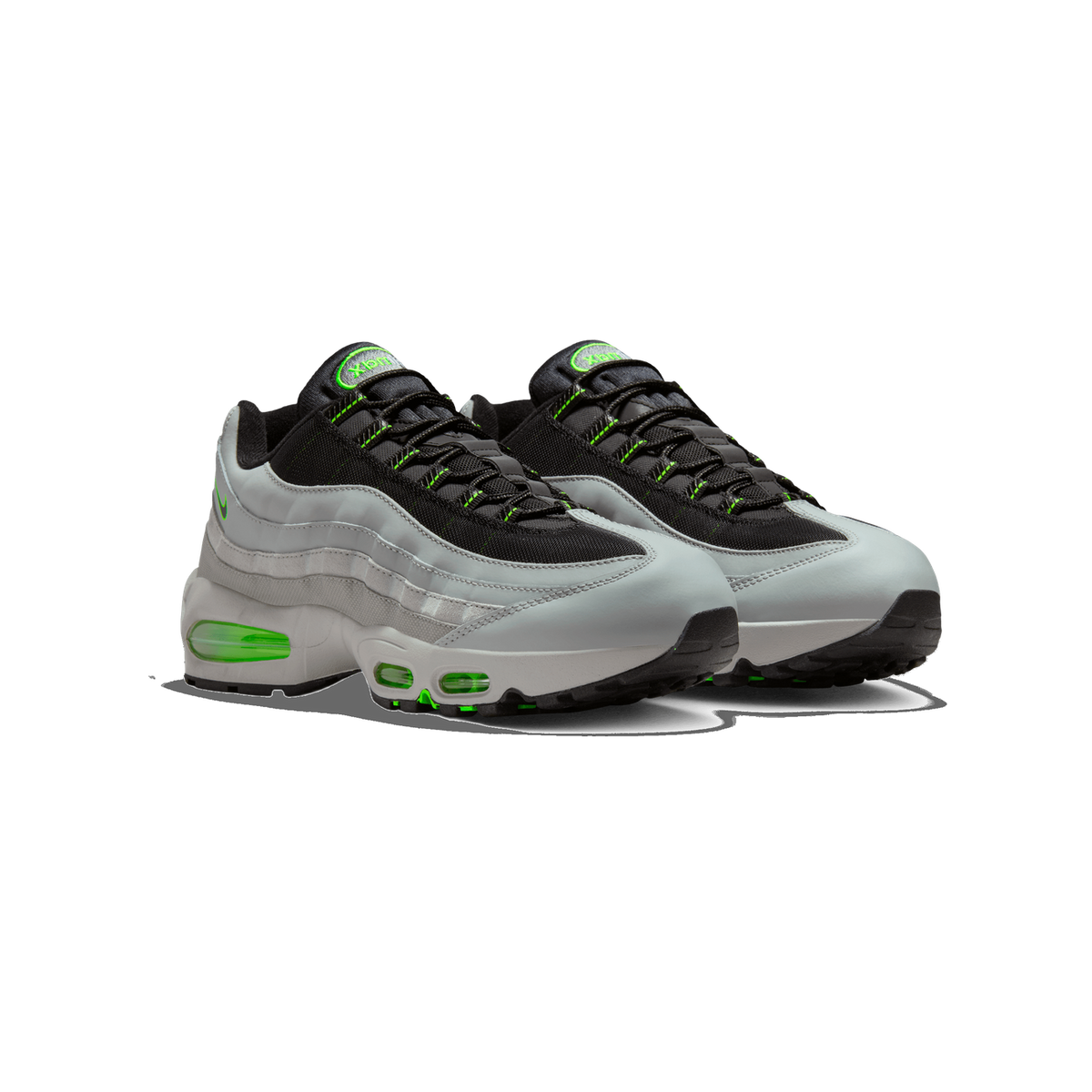A pair of grey and black Nike Air Max 95 sneakers with bright green accents, shown side by side angled toward the left, with visible green Air units in the midsole and green 'max' branding on the tongue tabs.