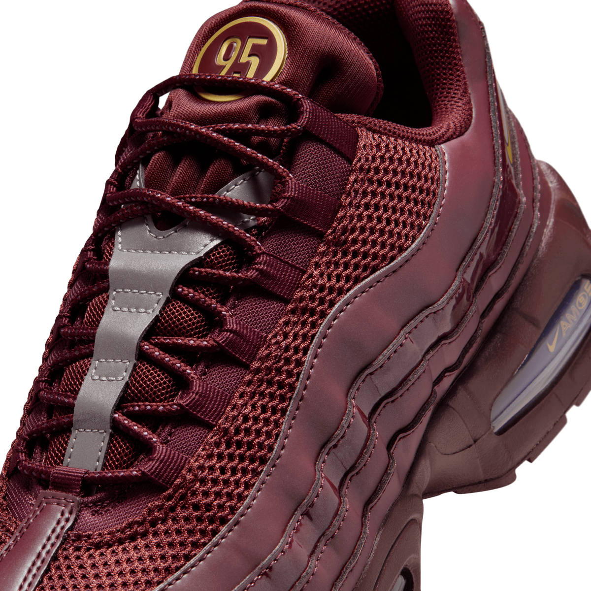 Close-up detail of a burgundy Nike Air Max 95 showing the laces, mesh panels, grey reflective overlay, gold-accented "95" heel tab, and the visible Air unit with "AIR MAX" lettering on the midsole.