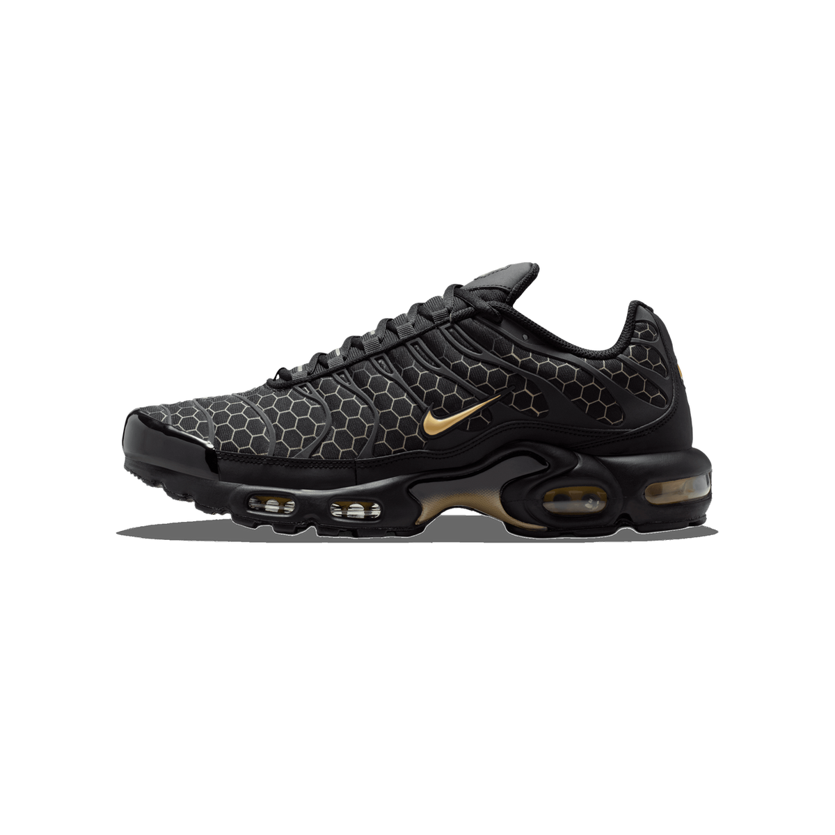 Side view of a black Nike Air Max Plus with gold Swoosh, honeycomb pattern overlays, and a visible Air cushioned heel unit, toe pointing left.
