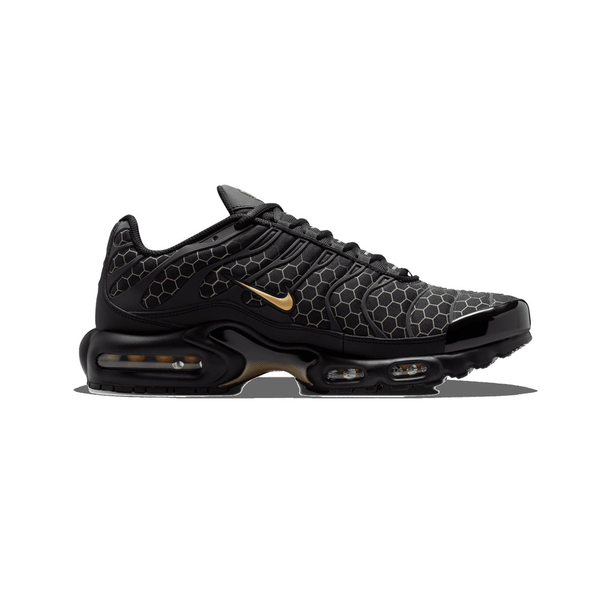 Side view of a black Nike Air Max Plus with honeycomb textured overlays, a gold swoosh, and a visible orange-tinted Air cushioning unit in the sole, toe pointing left.