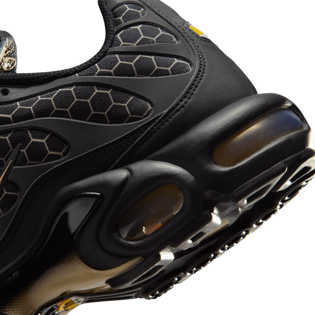 Close-up angled view of a black Nike Air Max Plus heel and Air cushioning unit with honeycomb textile paneling and honey-brown tinted air bubbles.