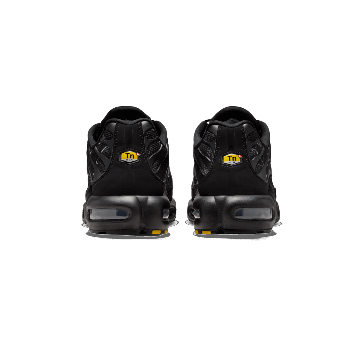 Rear view of a pair of black Nike Air Max Plus sneakers showing visible heel air units and yellow Tn Air logo tabs