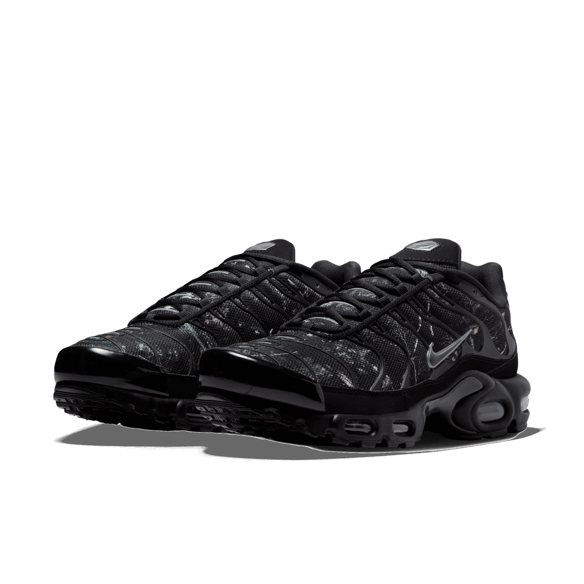 Pair of black Nike Air Max Plus sneakers with a mottled grey and black textured upper, viewed from the front at an angle showing both toe boxes and visible air cushioning in the heel
