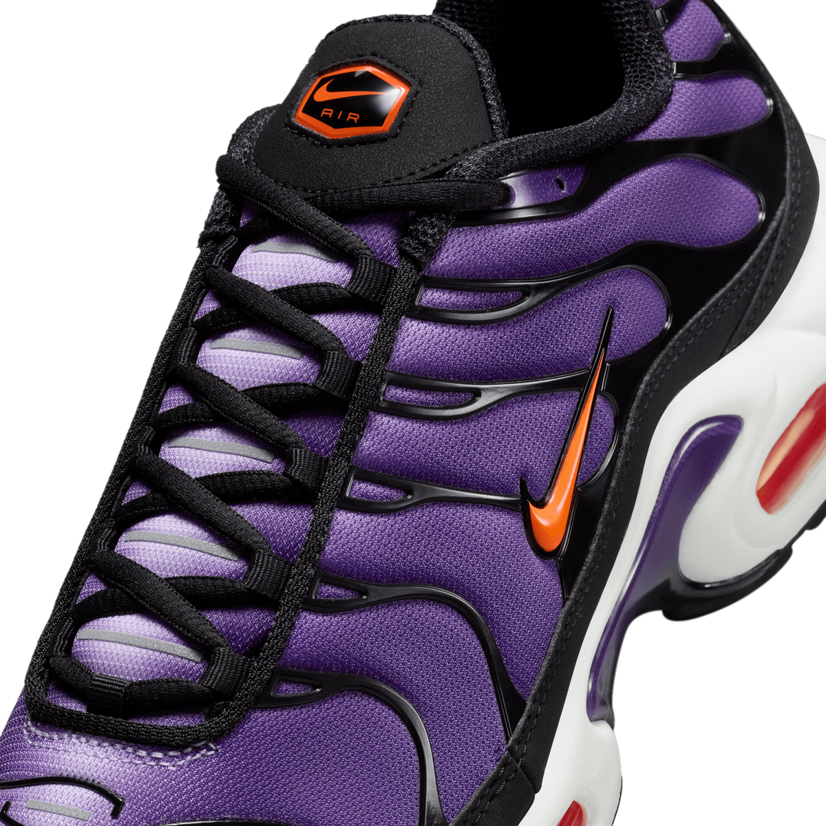 Close-up top view of a purple Nike Air Max Plus with black wavy overlays, orange swoosh, black laces, and a black tongue with an orange Nike Air tab.