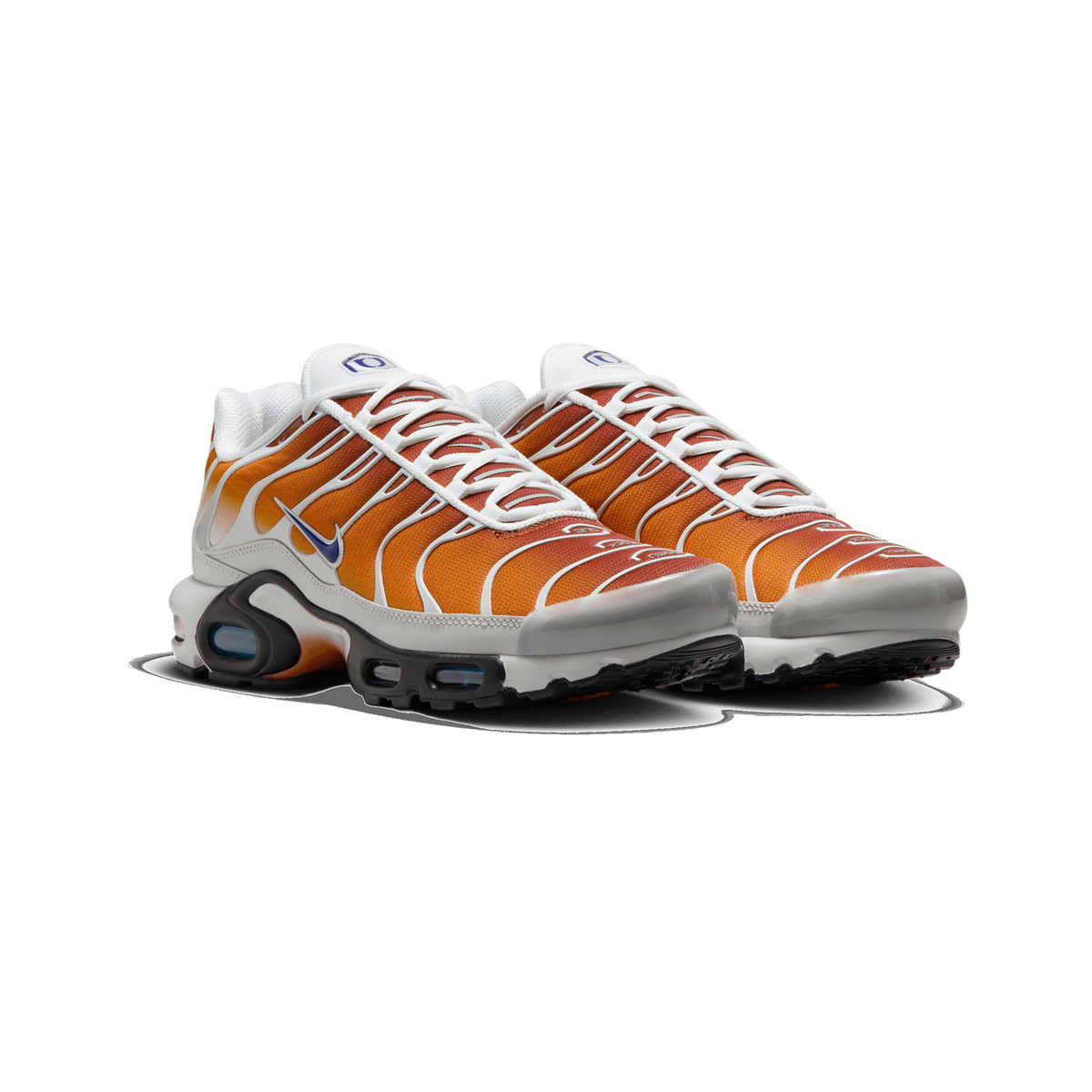 Pair of Nike Air Max Plus sneakers shown side by side at a front three-quarter angle, with orange-to-brown gradient mesh overlays, white laces and trim, grey toe caps, and a blue Swoosh logo on each shoe.