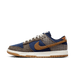 Lateral view of a Nike Dunk Low sneaker with navy corduroy panels, brown tweed and houndstooth fabric, a tan corduroy swoosh, and a gum rubber sole on a white midsole.