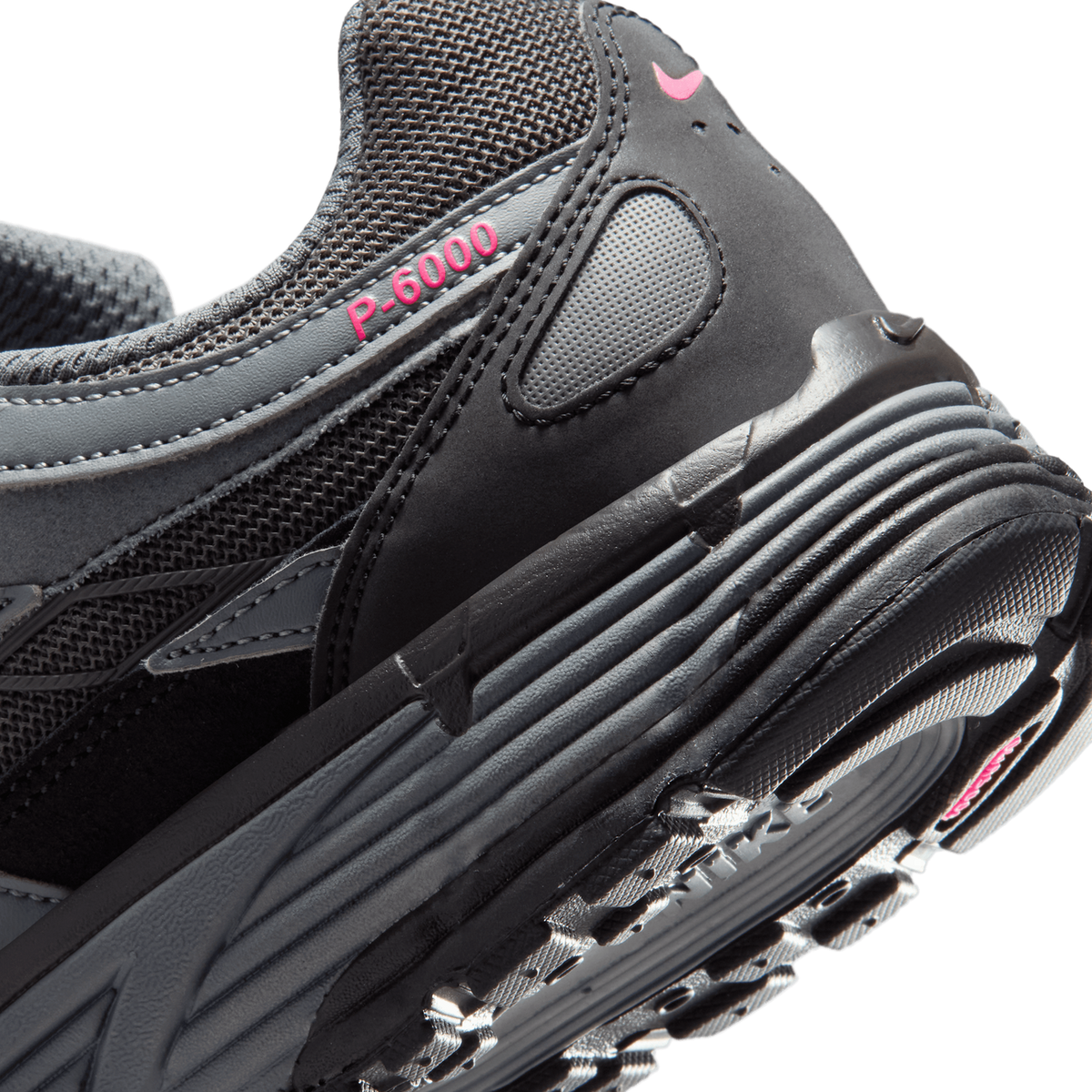 Close-up of the heel of a black and grey Nike P-6000 sneaker showing the pink P-6000 text and pink Swoosh on the heel tab, with the multi-layered rubber sole visible at the back.