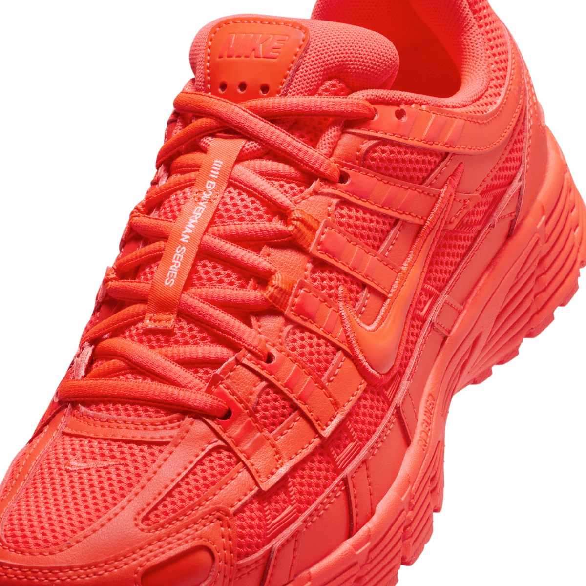 Close-up of a red-orange Nike P-6000 sneaker showing the tongue with a Nike logo, laces, mesh panels, overlays with Swoosh logos, and the lugged midsole, all in a monochrome bright crimson tone.