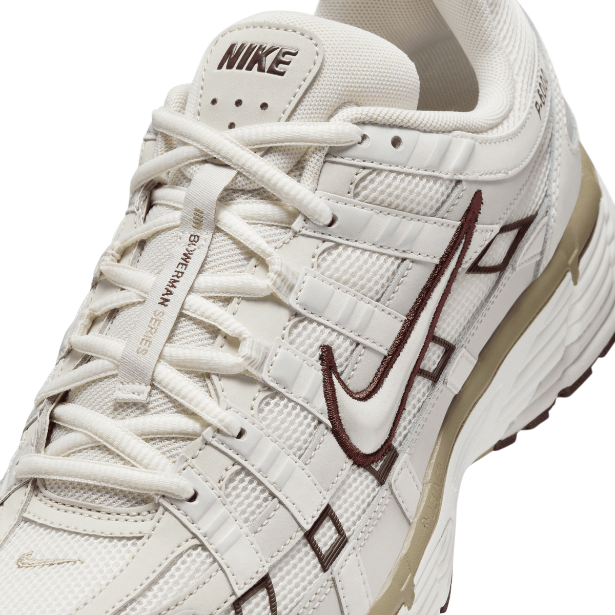 Close-up of the Nike P-6000 in cream and beige with brown embroidered Swoosh and NIKE heel-tab branding, showing the laces, mesh panels, and tan midsole.