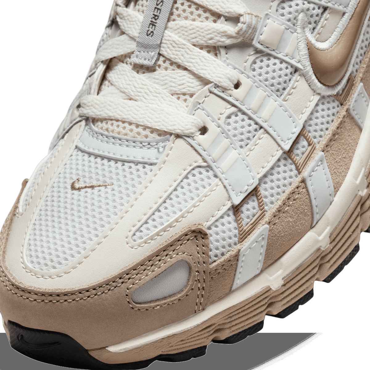Close-up detail of the toe box and lacing of a sneaker in cream, off-white mesh and tan suede, showing a small embroidered swoosh on the side panel, a tan swoosh on the tongue area, and a dark rubber outsole edge at the bottom.