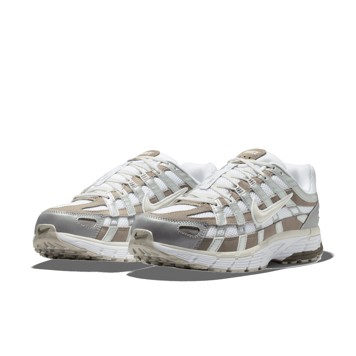 Pair of Nike P-6000 sneakers in white, taupe, and metallic silver with caged lacing straps, angled toward the front-left showing toe caps and chunky soles.