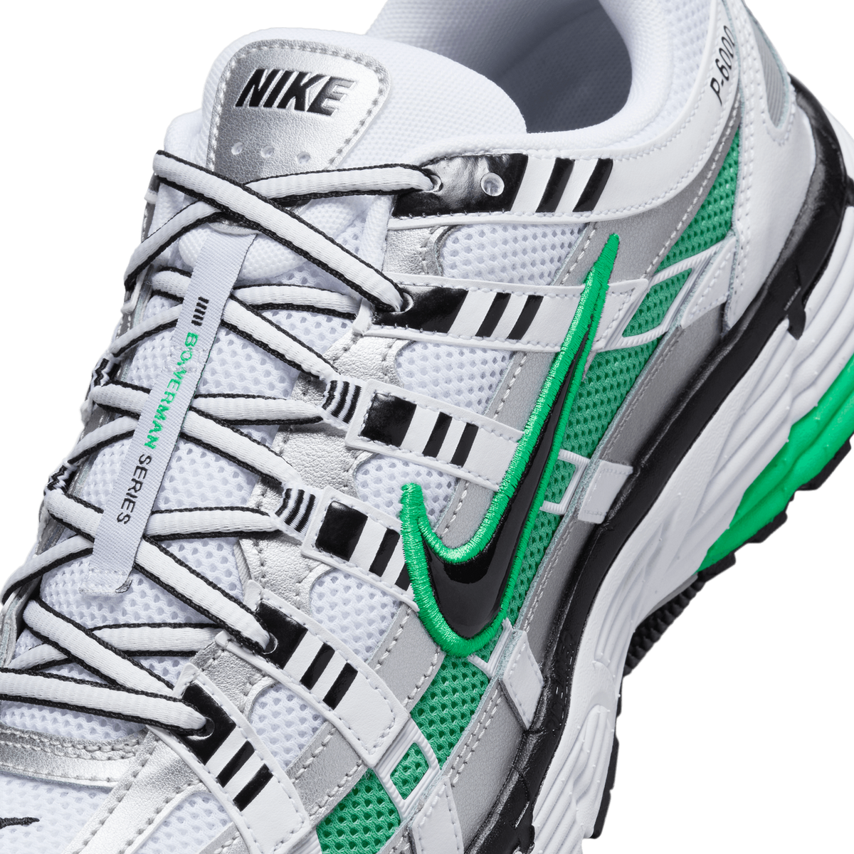 Close-up detail of a white, silver, green and black Nike P-6000 sneaker showing the NIKE heel tab, laced eyestays, a green and black embroidered Swoosh, and green mesh panels along the side.