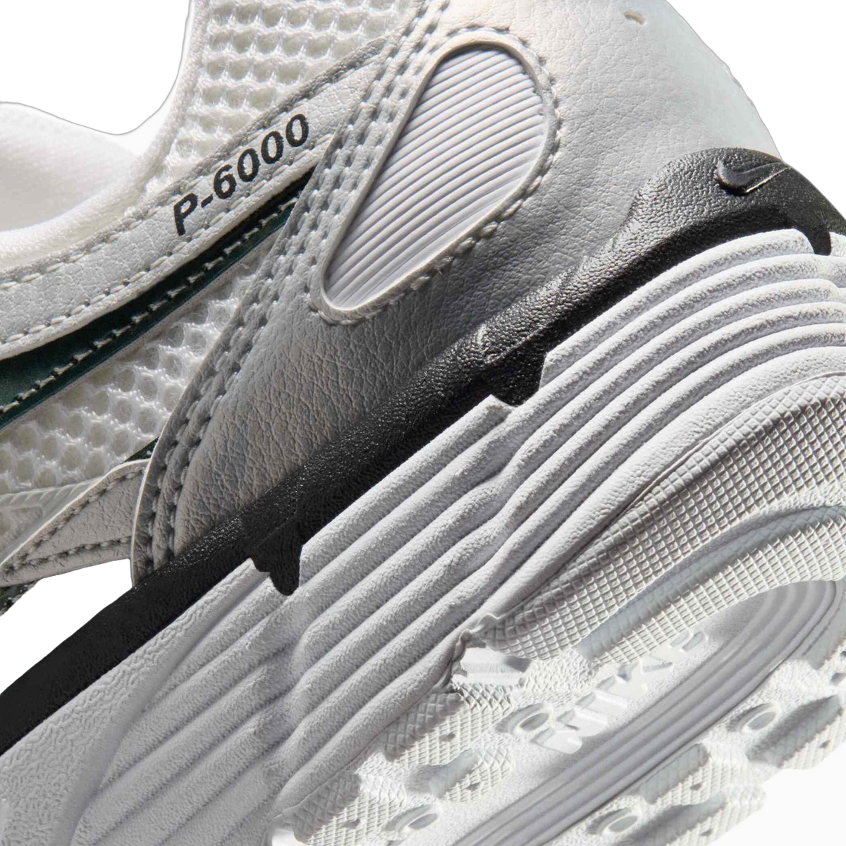 Close-up of the Nike P-6000 heel area showing the white mesh upper, ribbed leather panel, P-6000 text on the tongue, and layered midsole with visible Nike branding on the outsole.