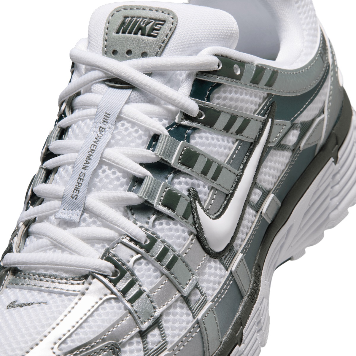 Close-up detail of a white and grey-green Nike P-6000 sneaker showing the heel tab with embossed NIKE logo, white laces, mesh panels, and the white Swoosh with dark green outline on the side overlays.