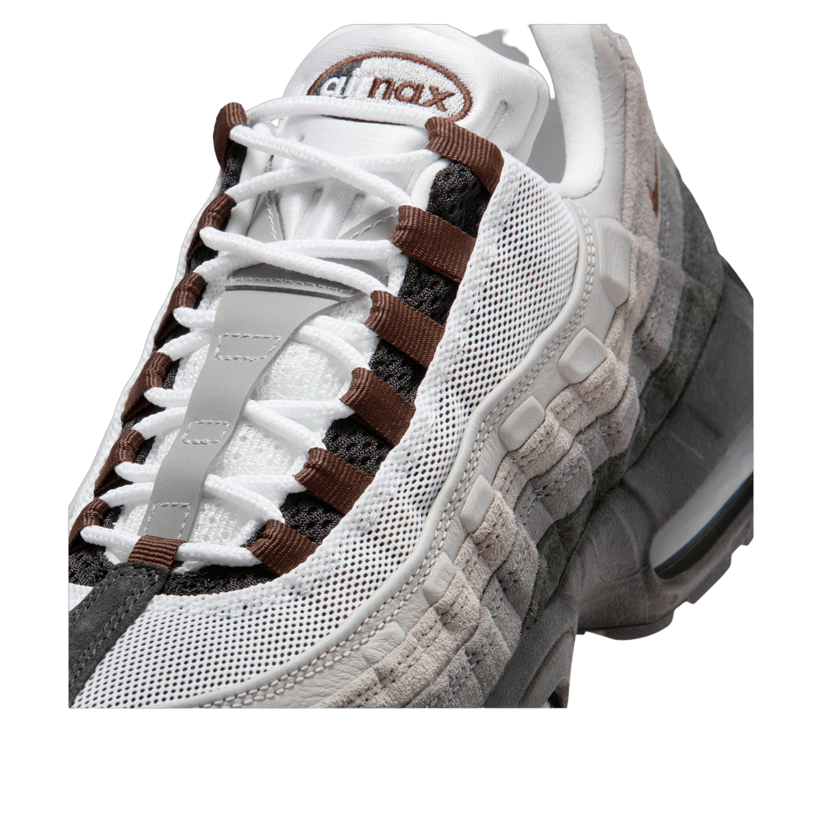 Close-up view of a Nike Air Max 95 sneaker's toe box and lacing, showing white mesh, brown eyelets and laces, grey suede overlays, and an Air Max tongue label.