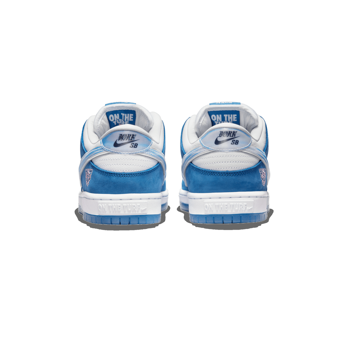 Rear view of a pair of blue and white Nike SB Dunk Low Born X Raised sneakers showing 'Born SB' heel tabs and 'On The Turf' text on the midsole