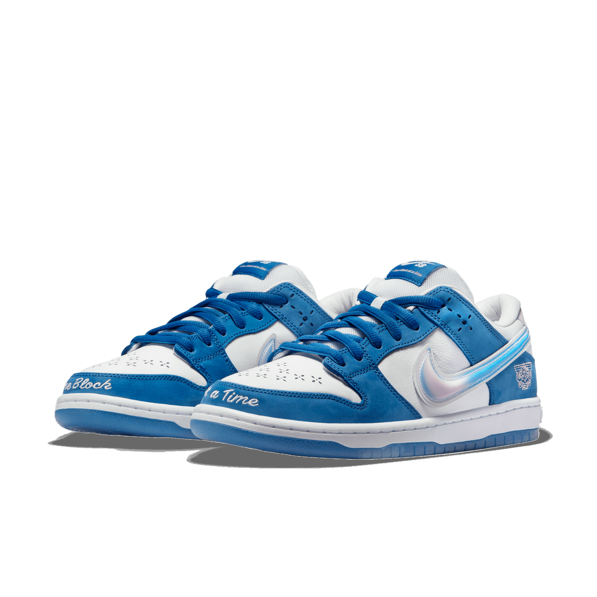 Pair of white and blue Nike SB Dunk Low Born X Raised sneakers with iridescent swoosh, embroidered text reading 'Block' and 'a Time', and a tiger graphic on the heel.