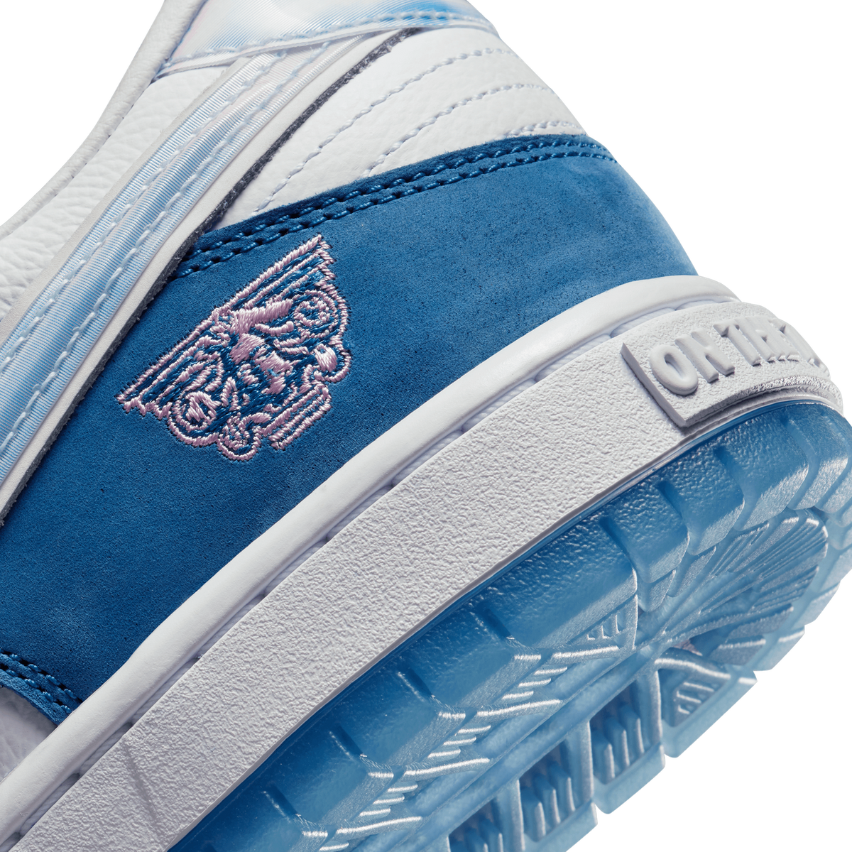 Close-up of the toe box of a navy and white Nike SB Dunk Low with an embroidered pink logo patch and textured blue outsole.