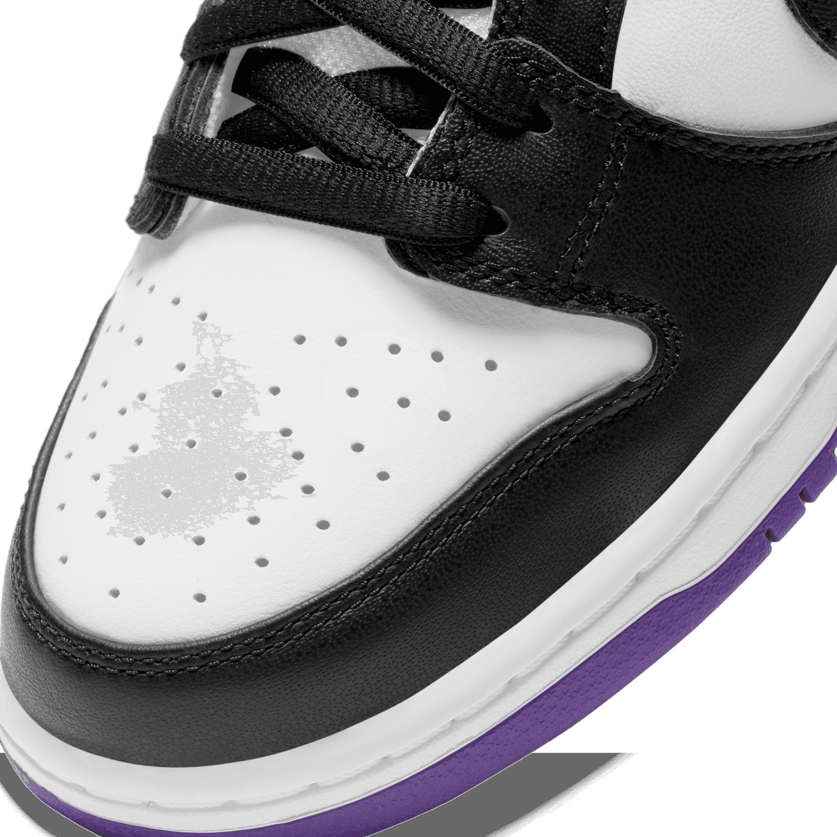 Close-up of the toe box of a black and white Nike SB Dunk Low with perforated holes and a purple midsole edge visible below