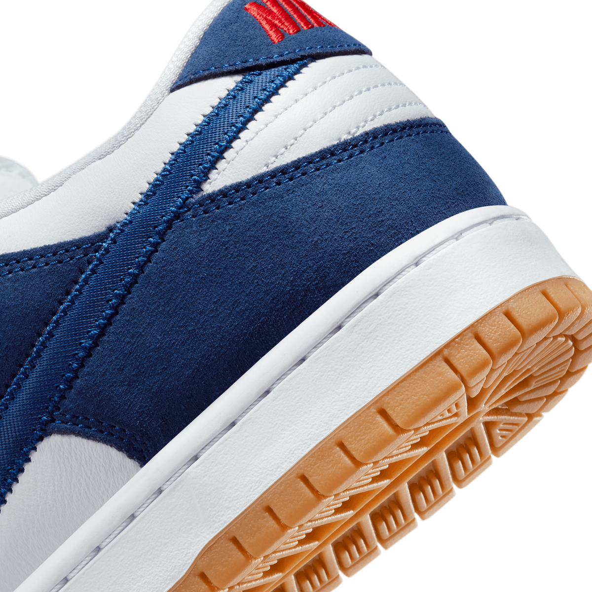 Close-up of a navy blue and white Nike SB Dunk Low showing the suede overlay, stitching, and gum rubber outsole with red embroidered text at the heel.