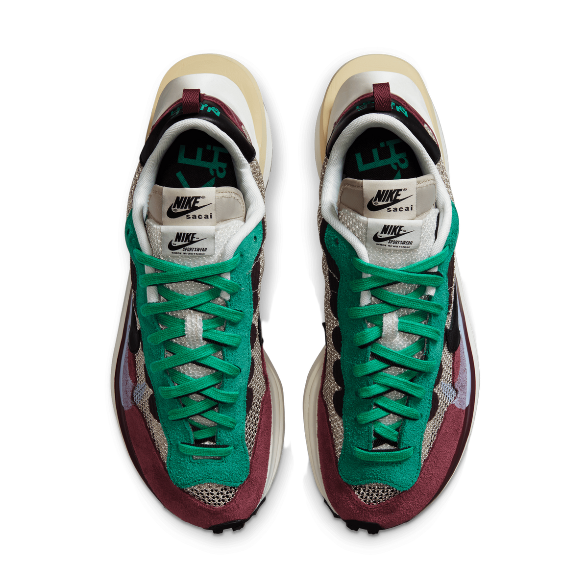Top-down view of a pair of Nike sacai Vaporwaffle sneakers placed side by side, showing green laces, green and maroon suede panels, beige mesh, and the tongue labels reading "Nike sacai" and "Nike Sportswear".