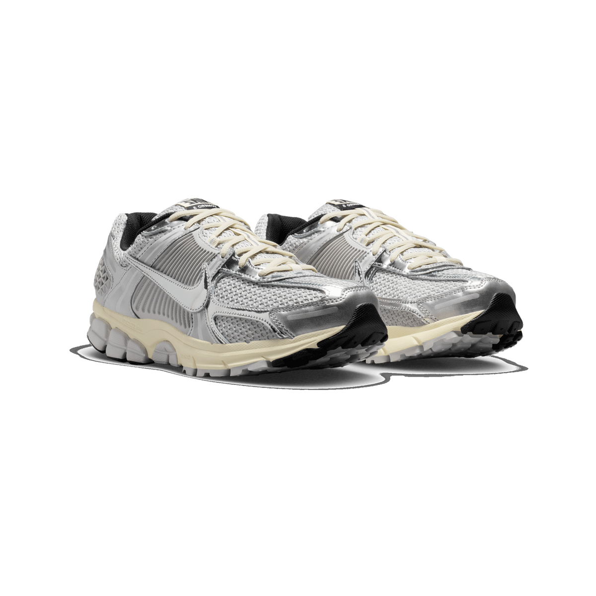 A pair of silver and light grey Nike Vomero 5 sneakers shown side by side at a three-quarter front angle, with metallic chrome overlays, mesh panels, cream laces and a cream and black sole.