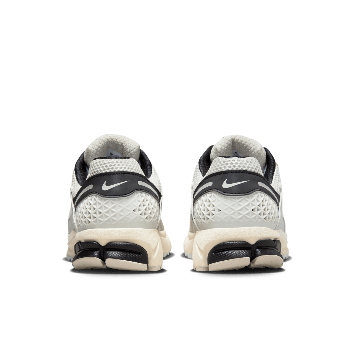 Rear view of a pair of Nike Zoom Vomero 5 sneakers in light bone and black with a cream textured midsole and black heel tabs featuring the Nike swoosh.