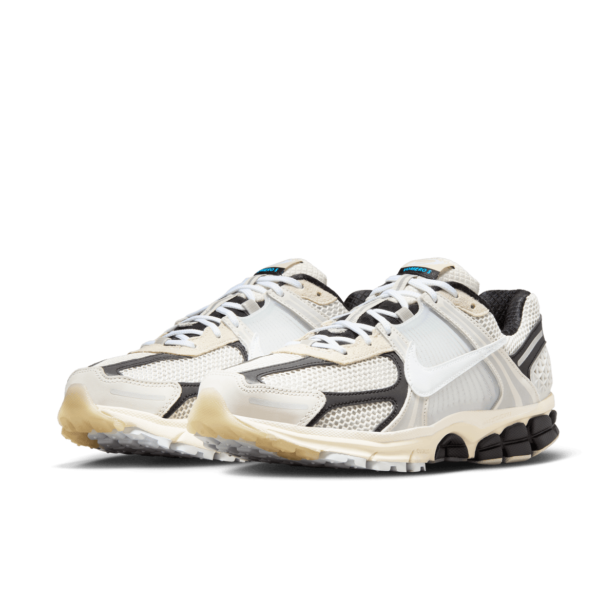 Front angled view of a pair of Nike Zoom Vomero 5 sneakers in light bone and black with white laces and mesh paneling on segmented cream and black midsoles