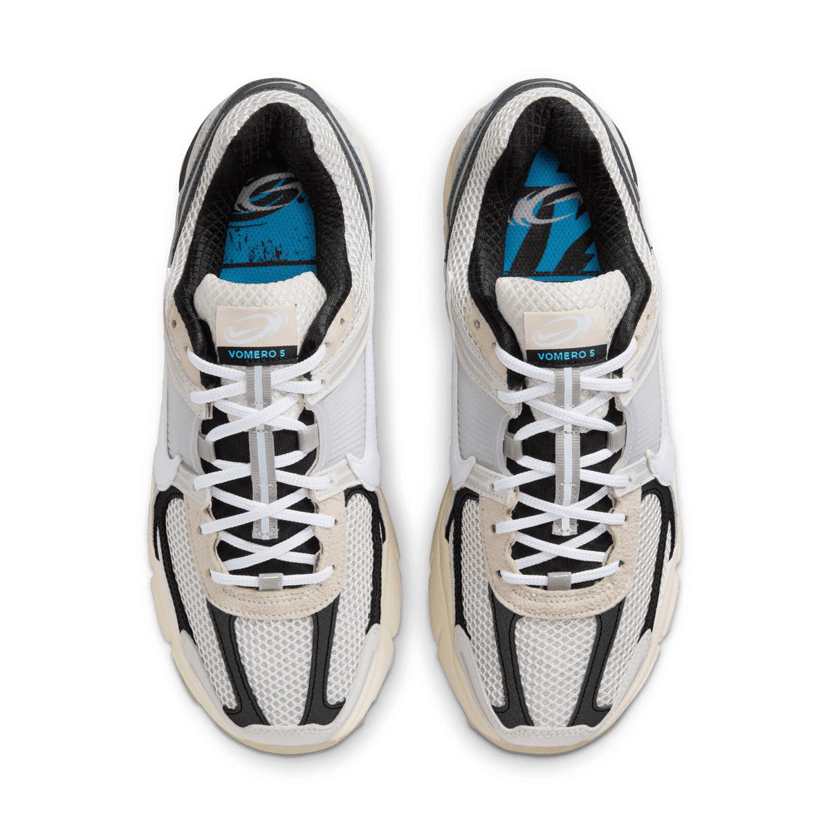 Top-down view of a pair of Nike Zoom Vomero 5 sneakers in light bone and black with white laces, mesh paneling, and a blue graphic tongue lining labeled Vomero 5