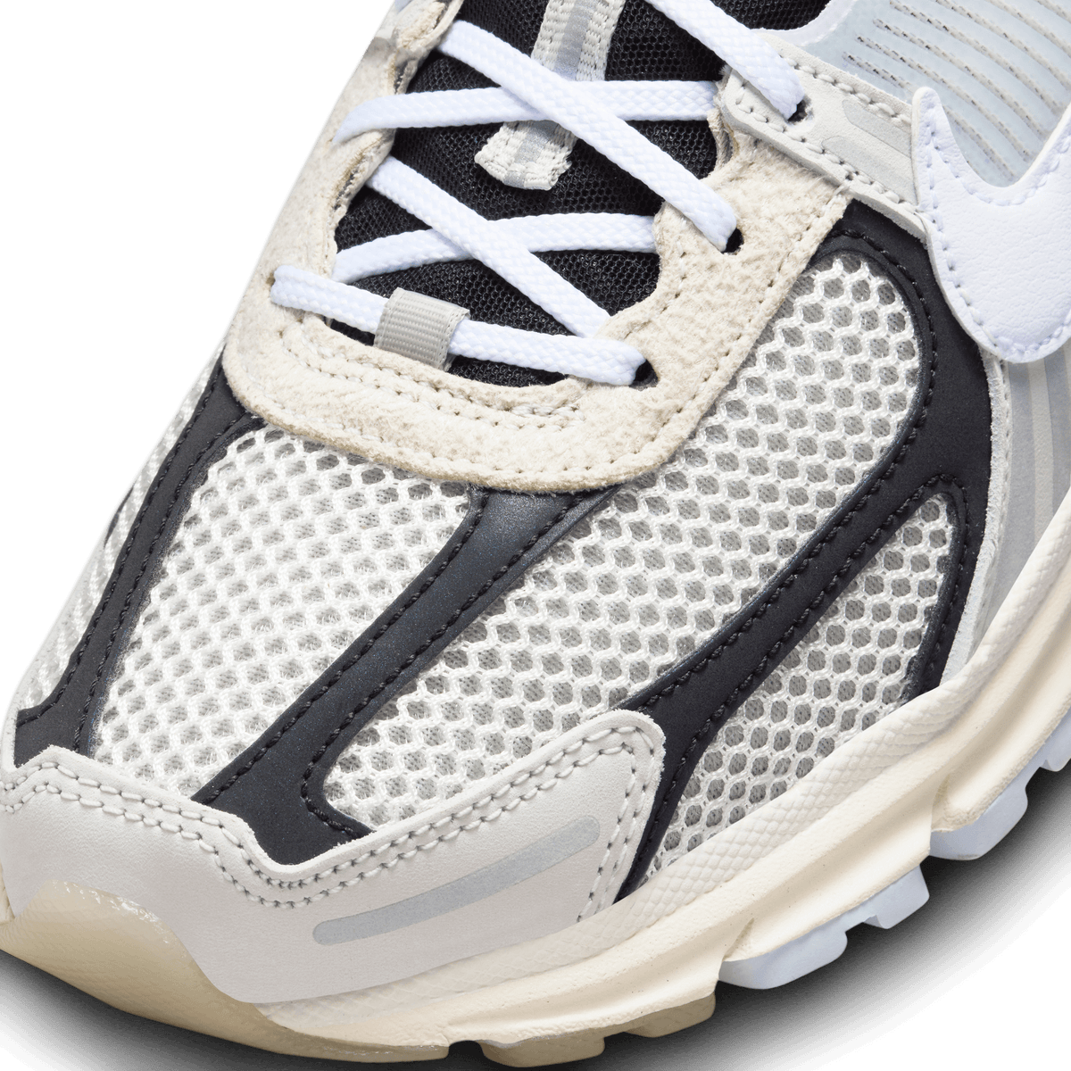 Close-up of the toe box of a Nike Zoom Vomero 5 sneaker showing white mesh panels, black overlays, and cream trim with white laces
