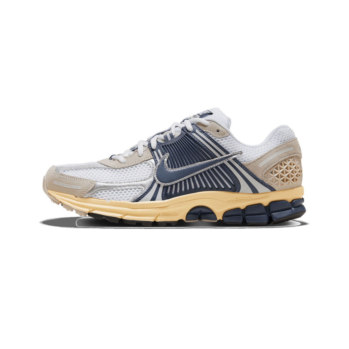 Left Nike Zoom Vomero 5 sneaker shown from the outside with toe pointing left, featuring white mesh upper, navy blue overlays, beige suede accents, a cream midsole, and navy outsole.