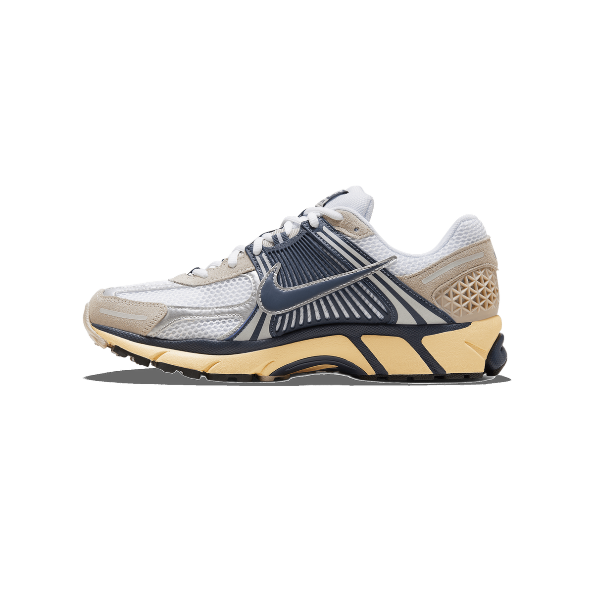 Lateral view of a white and navy Nike Zoom Vomero 5 with tan suede panels and a pale yellow outsole, toe pointing left