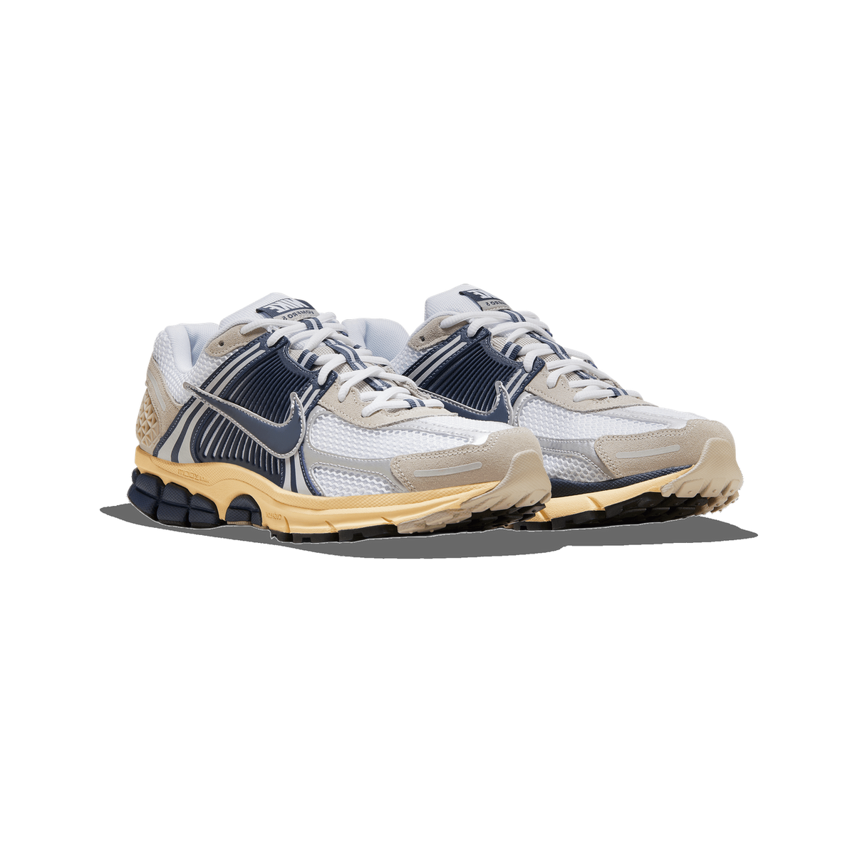 Pair of Nike Zoom Vomero 5 sneakers in white mesh with navy blue accents, tan suede overlays, and a cream midsole with black outsole, angled toward the left.