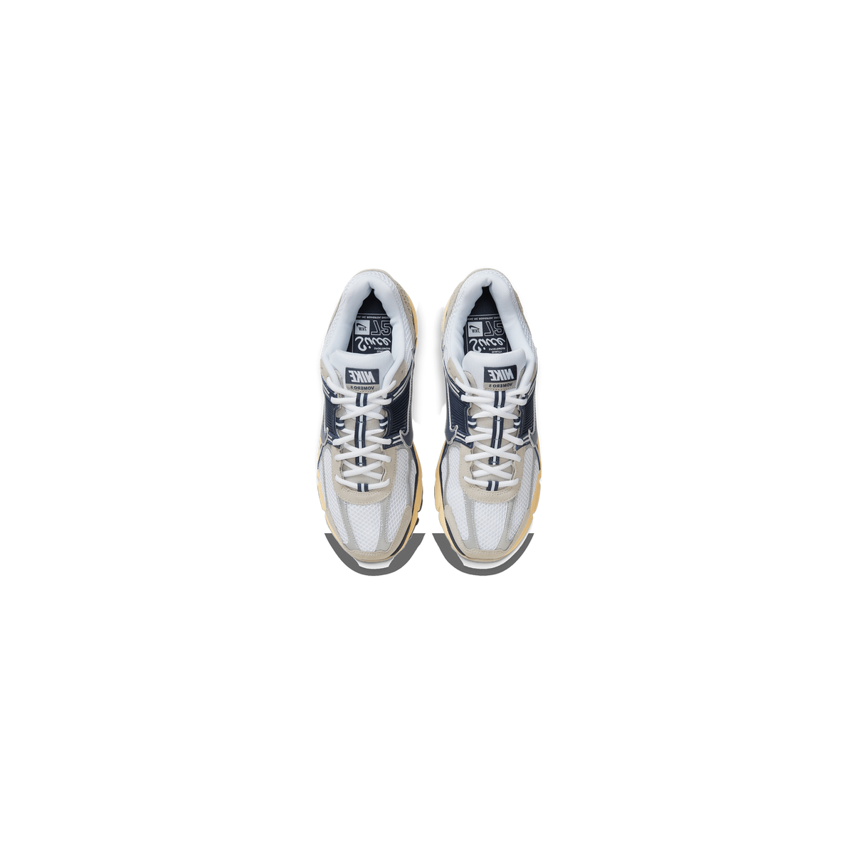 Top-down view of a pair of Nike Zoom Vomero 5 sneakers in white, navy, and cream with tan outsoles and Nike Vomero 5 branding on the tongues.