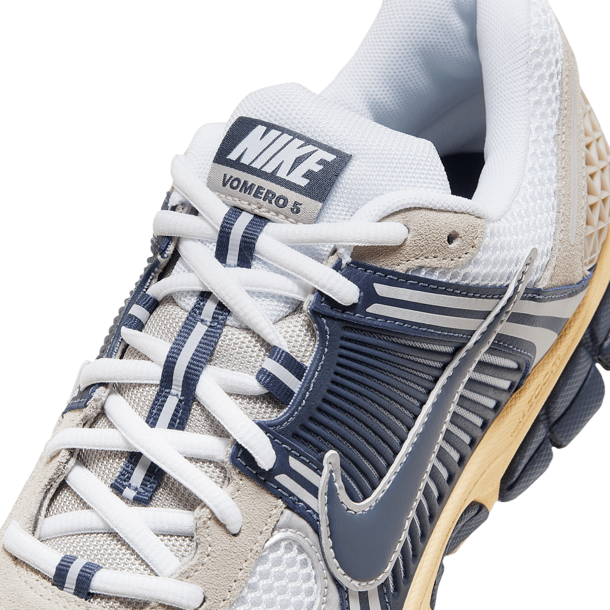 Close-up of a Nike Zoom Vomero 5 sneaker toe box and lacing area showing the navy Swoosh, ribbed overlay, white laces and the Vomero 5 tongue tag.