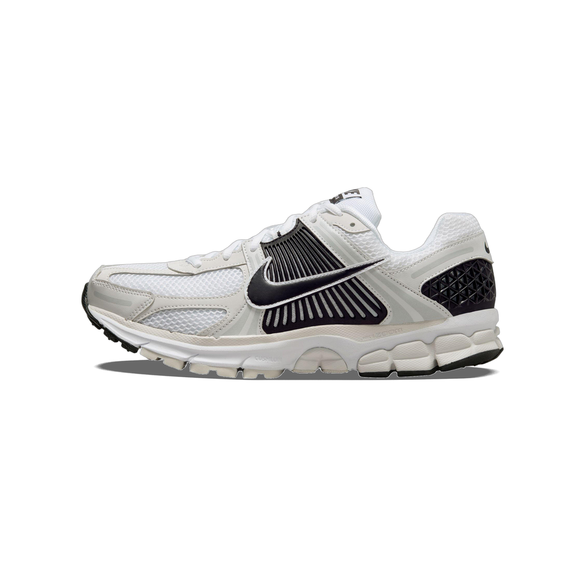 Side view of a white Nike Zoom Vomero 5 sneaker with black swoosh, black ribbed overlay, grey accents and a chunky white midsole, toe pointing left