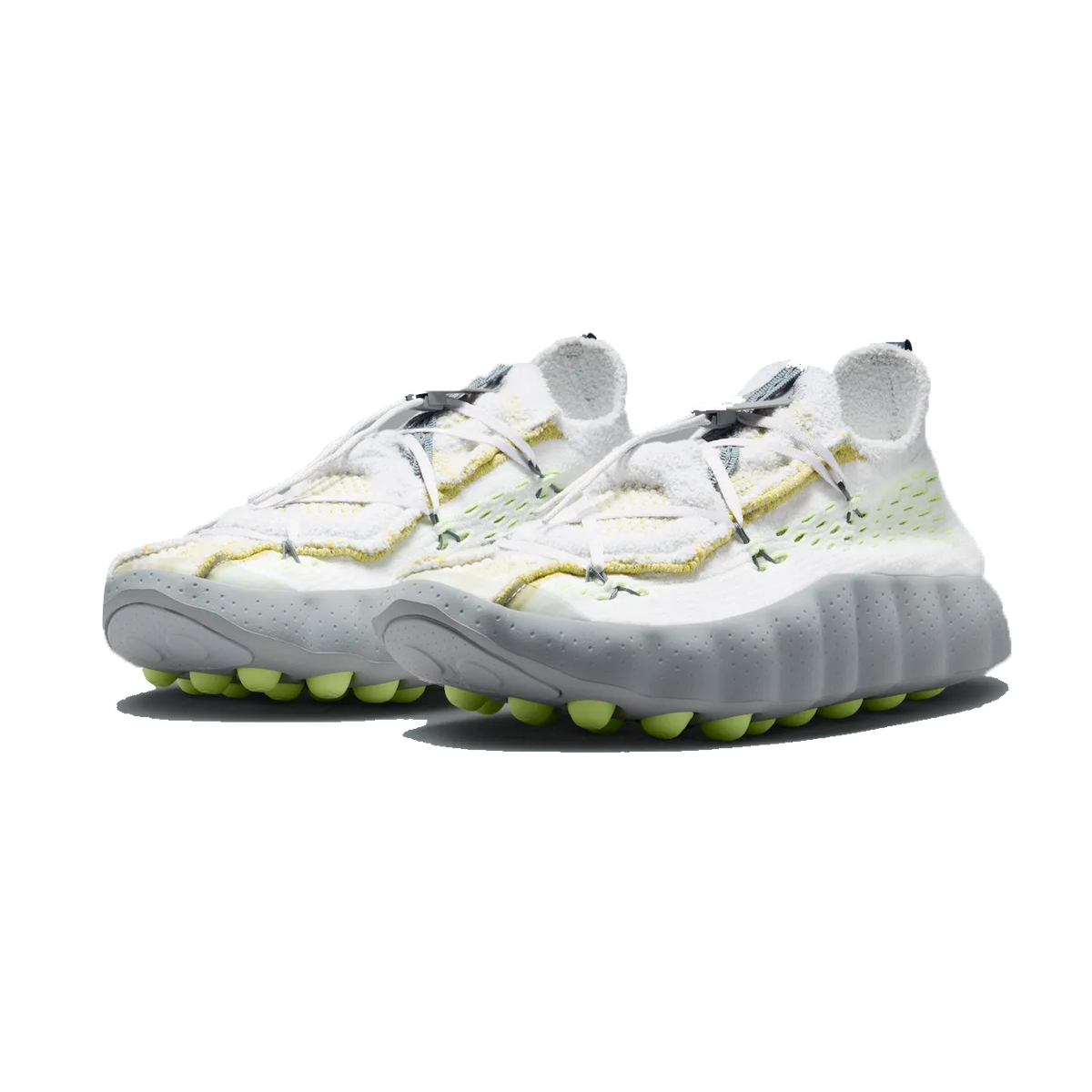 Pair of Nike Mind 002 Flyknit sneakers in white with yellow accents, grey textured outsoles, and volt-colored nub details, shown from a front-angled view.
