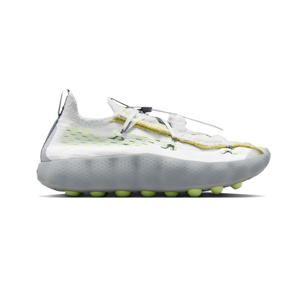 Side view of a white Nike Mind 002 Flyknit sneaker with grey heel, yellow lace detailing, volt accents, and a grey rubber sole with rounded volt-colored traction nubs.