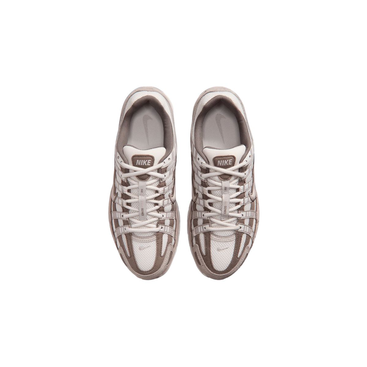 Pohled shora na pár tenisek Nike P-6000 ve smetanové a taupe barvě s klecovými kryty a křížem vedenými tkaničkami.