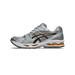 Side view of a silver and black Asics Gel-Kayano 14 running shoe with gold accents on the sole, toe pointing right