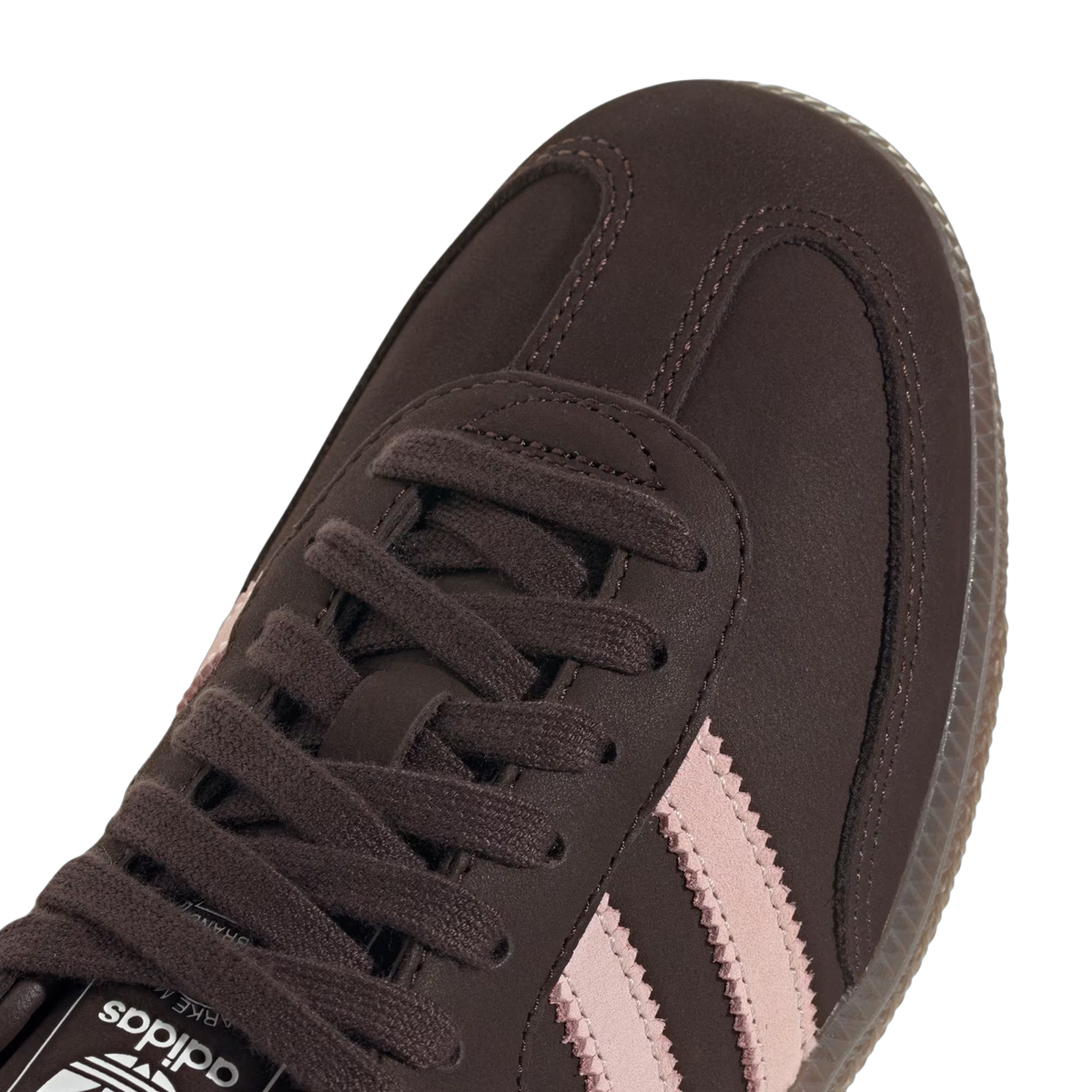 Close-up macro view of a brown Adidas Samba OG sneaker toe box showing the laces, stitched overlays, and pink serrated three-stripe branding.