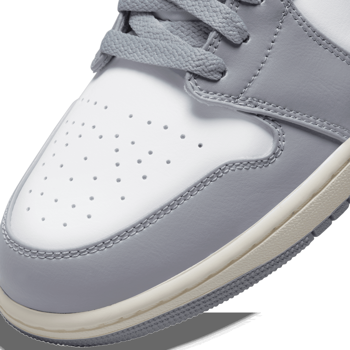 Close-up of the toe box of a gray and white Air Jordan 1 Low showing perforated leather, stitching, and cream midsole detail.