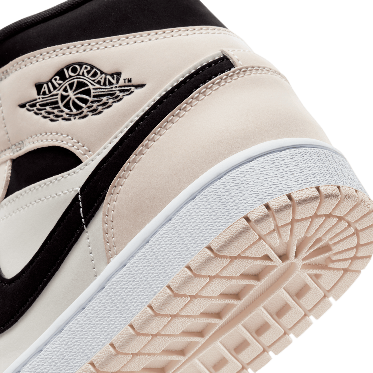 Close-up of the heel and outer side of a high-top sneaker showing a Jumpman-style Air Jordan wings logo embossed in black on a light beige panel, black overlay trim, white midsole edge, and a beige rubber outsole with a tread pattern.