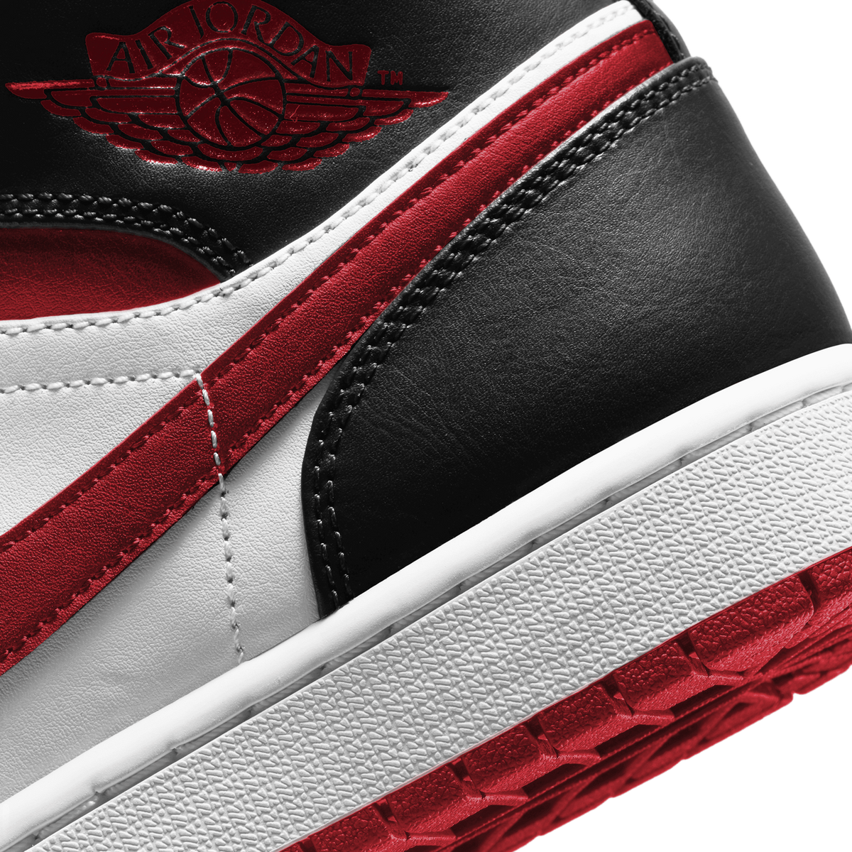 Close-up of the Air Jordan 1 Mid in gym red, black, and white showing the Wings logo on the ankle and the midsole stitching detail.