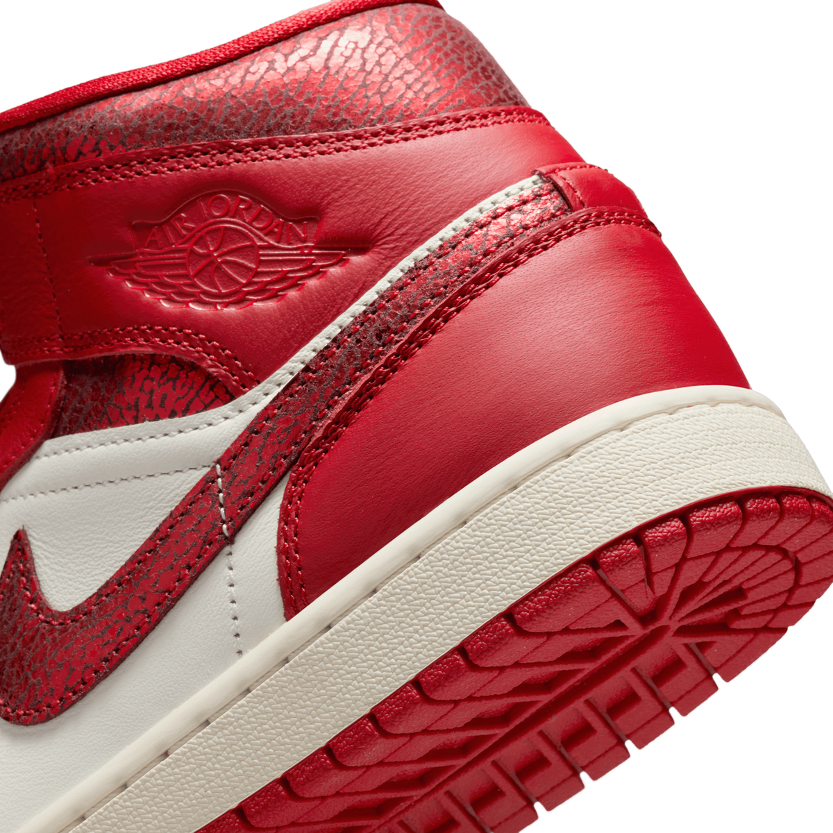 Close-up angled view of a red and white Air Jordan 1 Mid showing the cracked leather texture, Nike Swoosh, Wings logo on the ankle, and red rubber outsole.