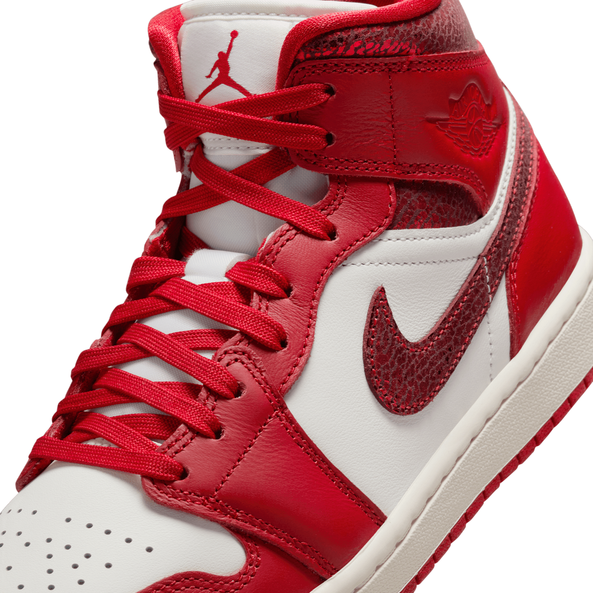 Close-up angled view of a white and red Jordan 1 Mid sneaker showing the crackled leather ankle collar, red laces, Swoosh, and Jumpman logo on the tongue.