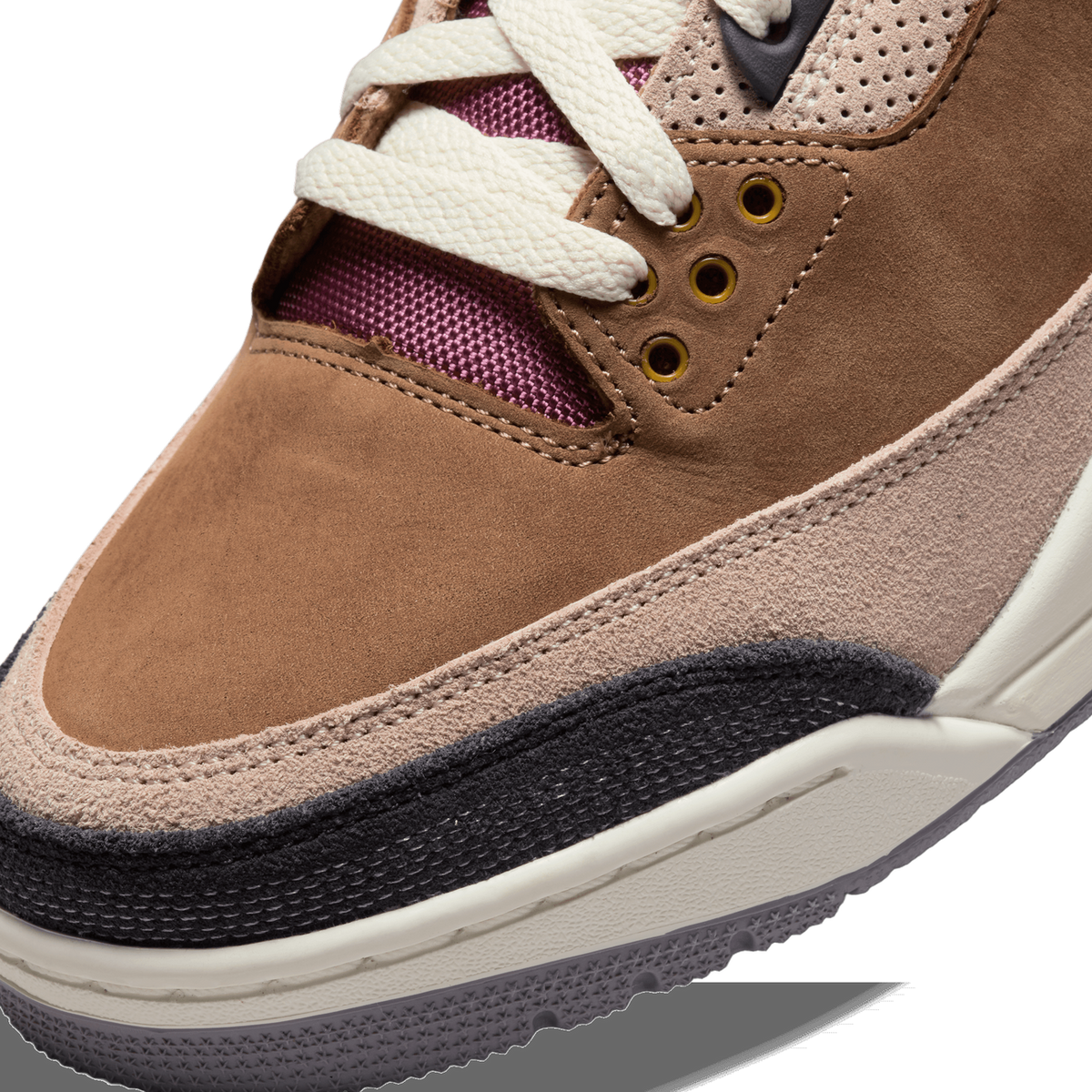 Close-up of the toe box and lacing of a brown Air Jordan 3 sneaker, showing brown suede overlays, beige suede panels, a black toe bumper, cream laces, gold eyelets and a burgundy mesh tongue visible beneath the laces.