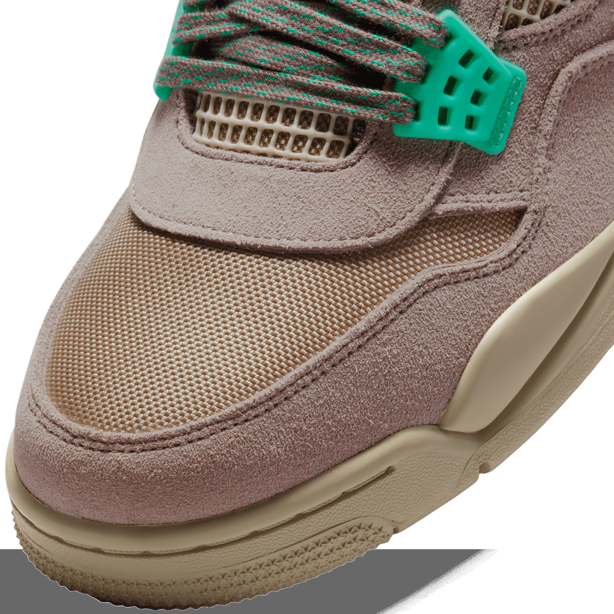 Close-up of the toe box and lace area of a taupe suede sneaker with tan mesh panels, brown laces with green stitching, a green plastic lace lock, and a tan rubber midsole and outsole edge.