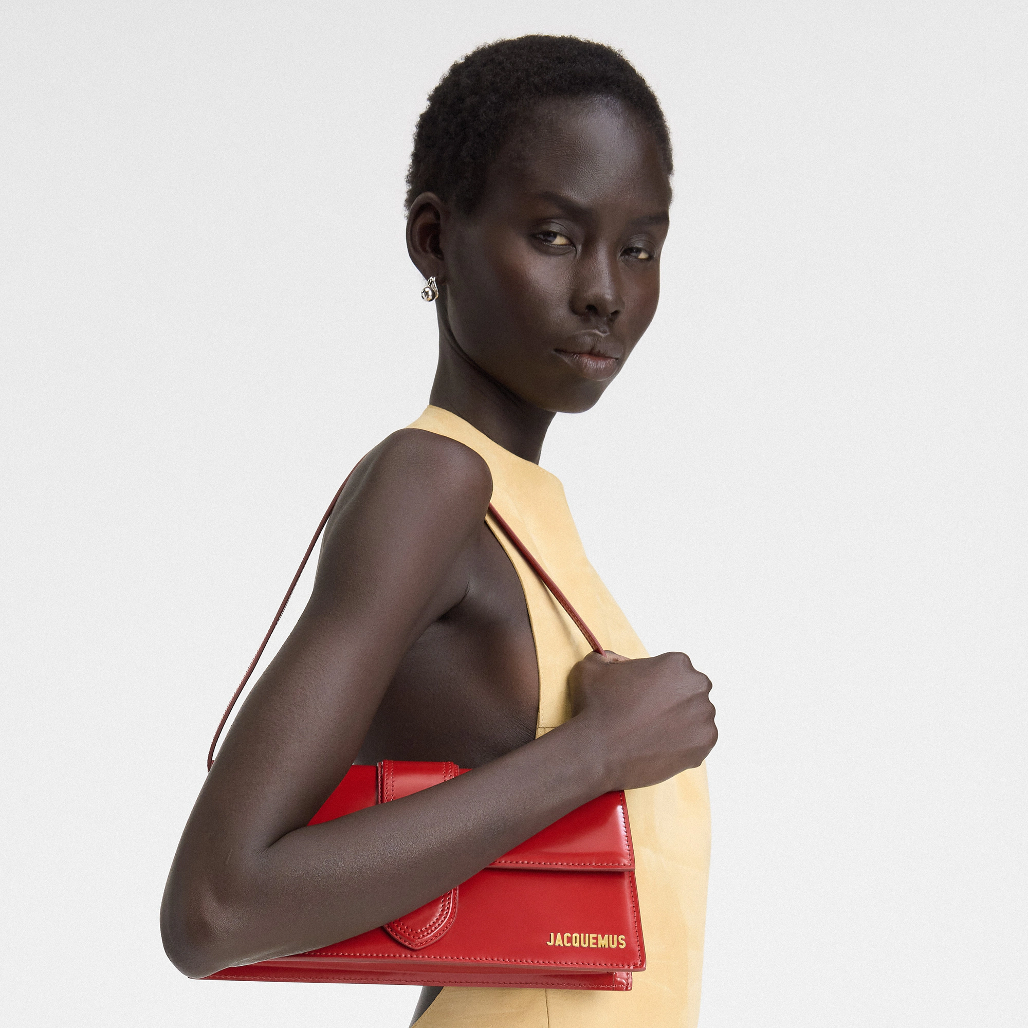 Woman holding a red handbag with 'Jacquemus' branding against a light gray background