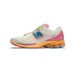 Side view of a New Balance 1906R sneaker with a white mesh upper, blue N logo, pink heel accents, and an orange, pink and red multicolor midsole, toe pointing left.